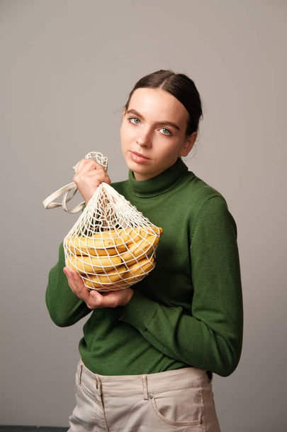 teen girl holding string bag with bananas in home interior - Fotografie, Obrázek