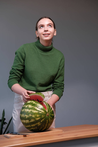 young woman cutting ripe watermelon in home interior - Foto, afbeelding