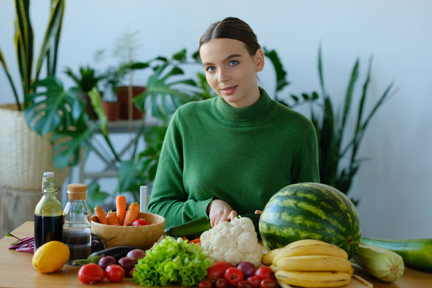 young woman cutting fresh vegetables in home interior - Foto, afbeelding