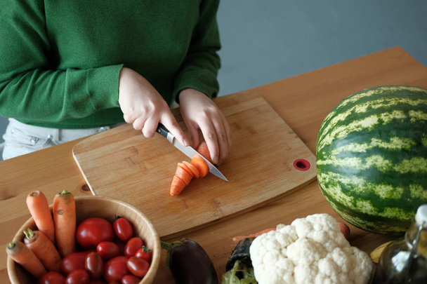 cropped view of woman cutting carrots on wooden board in home interior - Foto, Imagem