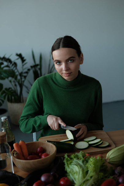 young cheerful girl cutting zucchini in home interior - Zdjęcie, obraz