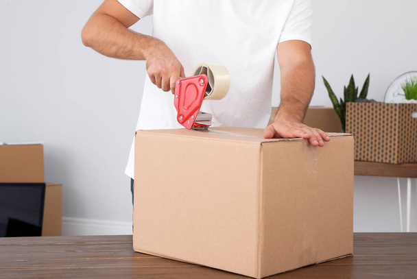 Young worker packing cardboard box in room, closeup. Moving service - Fotoğraf, Görsel