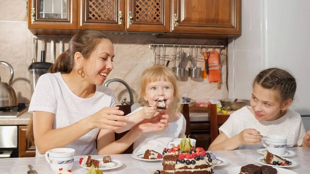 ママと二人の娘がキッチンで手作りのチョコレートケーキとお茶を持っている、家で家族の誕生日. - 写真・画像
