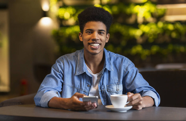 Cheerful black teen guy drinking coffee at cafeteria - Foto, imagen