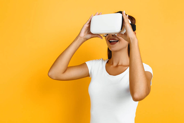 Young beautiful girl in virtual reality glasses on yellow backgr - 写真・画像