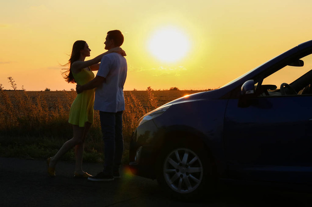 Sylwetka szczęśliwej pary w pobliżu nowego samochodu w krajobrazach o zachodzie słońca - Zdjęcie, obraz