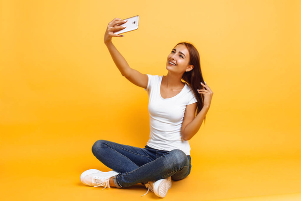 Young girl in white t-shirt sitting cross-legged and taking self - Фото, зображення