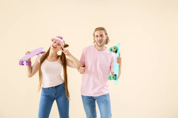 Cool young couple with skateboards dancing against light background - Photo, Image