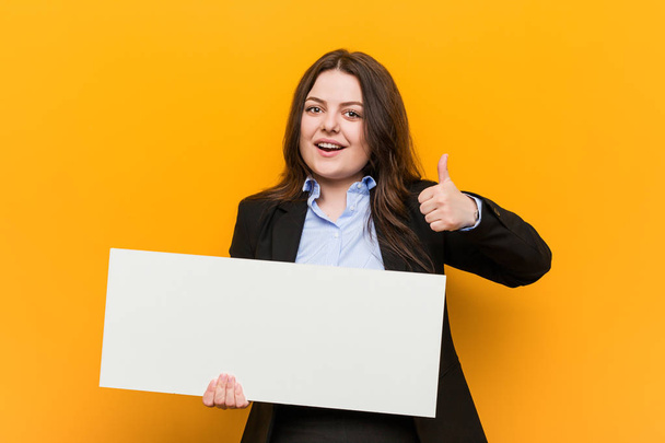 Fiatal és méretű kanyargós nő, aki egy plakát, mosolyogva emelése hüvelykujj fel - Fotó, kép
