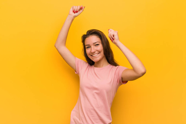 Молодая европейская женщина изолирована на желтом фоне празднуя особый день, прыгает и поднимает руки с энергией
. - Фото, изображение