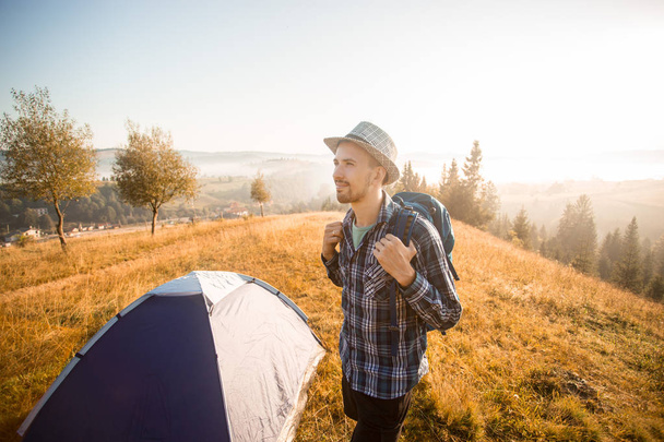 Красивий бородатий турист досліджує нові місця на вершині гір. Пішохідний чоловік в капелюсі з рюкзаком щасливий побачити осінній схід сонця
 - Фото, зображення