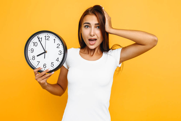 Portrait of a shocked girl holding a watch, girl overslept in th - Foto, Bild
