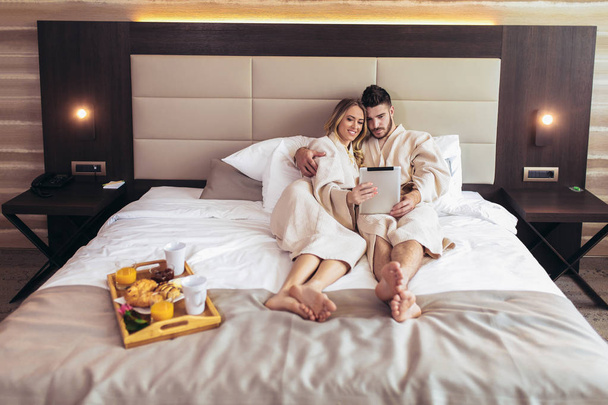 Happy couple using digital tablet while lying together in bed in - Fotó, kép