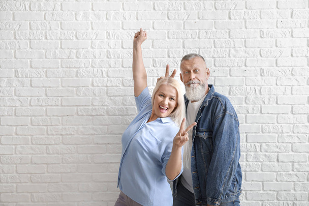 Feliz pareja madura mostrando el gesto de victoria contra la pared de ladrillo blanco
 - Foto, imagen