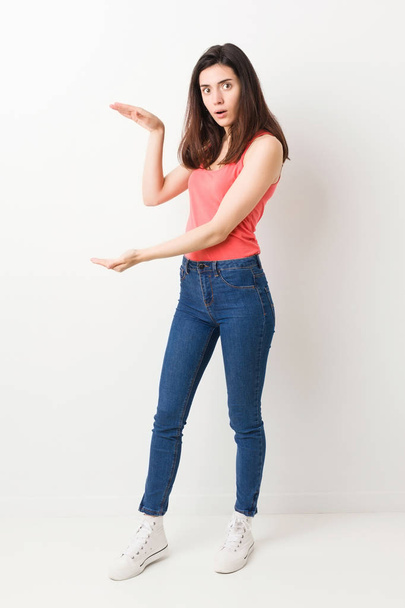 Full body young woman on white background shocked and amazed holding a copy space between hands. - Foto, immagini