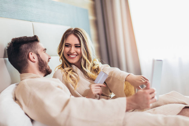 junges glückliches Paar shoppt online im Luxus-Hotelzimmer.  - Foto, Bild