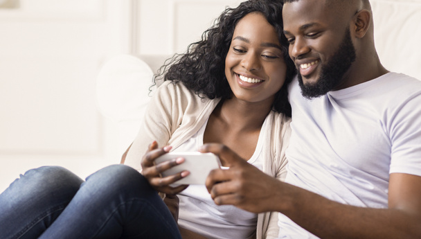 Gelukkig Afrikaans paar kijken naar grappige Video's op de smartphone thuis - Foto, afbeelding