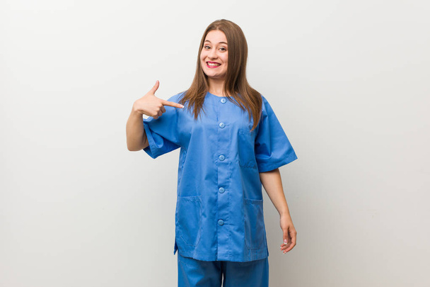 シャツのコピースペースに手で指差す白い壁の人に対する若い看護師の女性は、誇りと自信を持って - 写真・画像