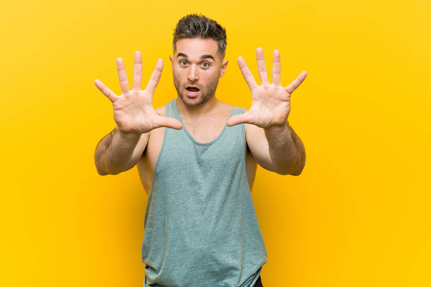 Młody człowiek fitness na żółtym tle pokazując numer dziesięć z rękami. - Zdjęcie, obraz