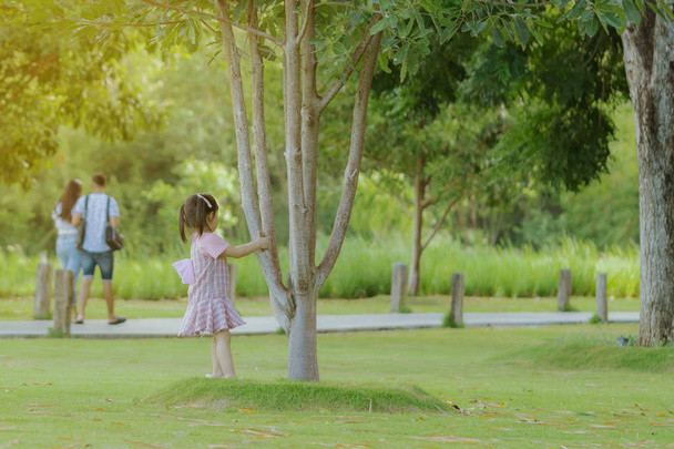 Dziewczynka w różowej spódnicy cieszy się relaksującym czasem grając na zielonym trawniku w publicznym parku wieczorem. - Zdjęcie, obraz