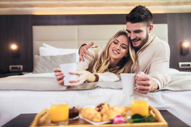 Νεαρό χαρούμενο ζευγάρι που έχει πρωινό στο πολυτελές δωμάτιο του ξενοδοχείου.  - Φωτογραφία, εικόνα
