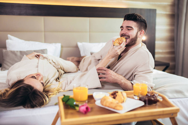 Молодая счастливая пара завтракает в роскошном номере отеля
.  - Фото, изображение