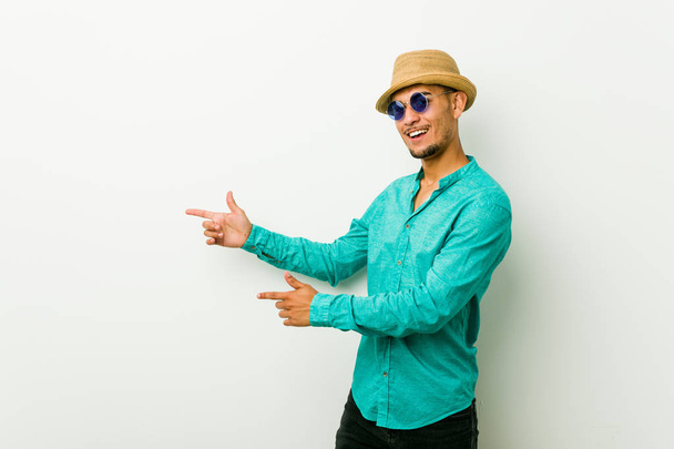 Young hispanic man wearing a summer clothes excited pointing with forefingers away. - Фото, изображение