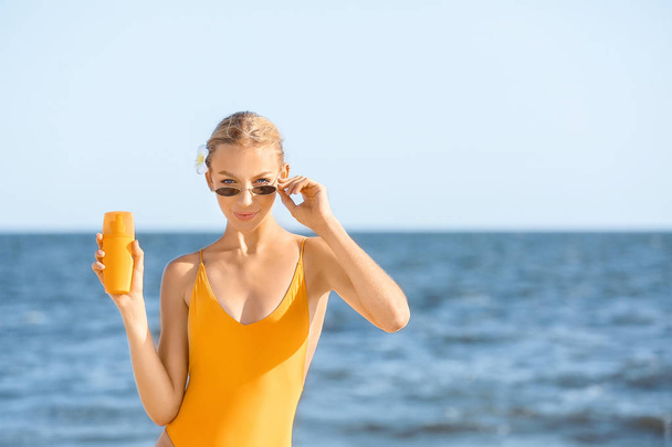 Beautiful young woman with sun protection cream on sea beach - Photo, Image