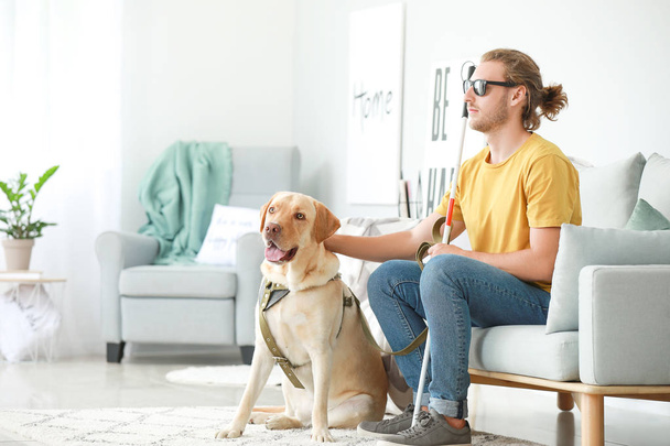 Jovem cego com cão guia em casa
 - Foto, Imagem