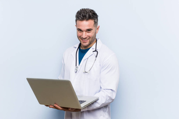 Caucásico médico hombre sosteniendo un portátil sonrisas alegres apuntando hacia el frente
. - Foto, imagen