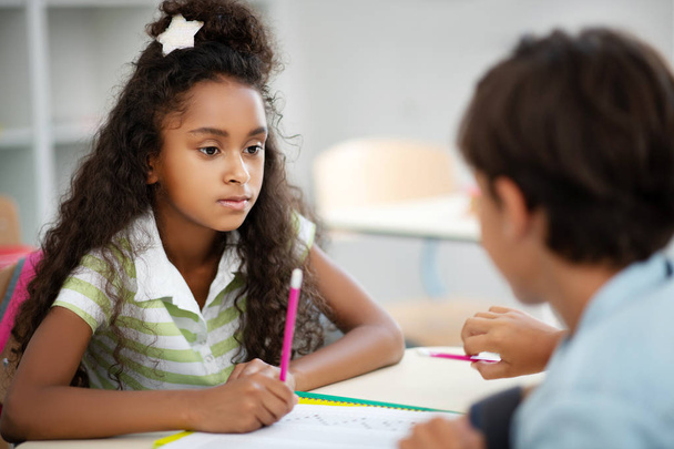 Cute dark-eyed girl listening to classmate while discussing test - Photo, image