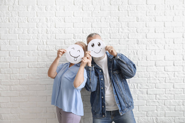 Casal maduro escondendo rostos atrás de emoticons contra parede de tijolo branco
 - Foto, Imagem