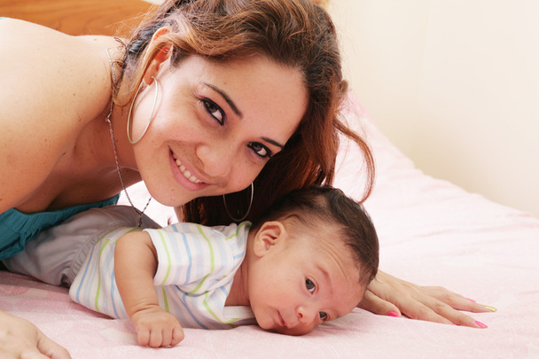 Mãe hispânica deitada na cama e segurando seu filho bebê
 - Foto, Imagem