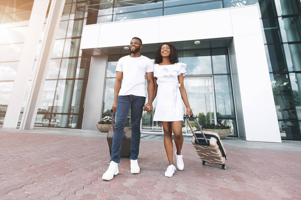 Feliz casal preto indo com bagagem fora do edifício do aeroporto
 - Foto, Imagem