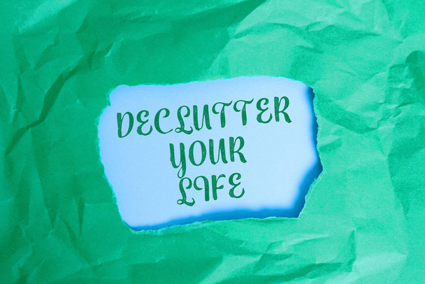 Text sign showing De Clutter Your Life. Conceptual photo remove unnecessary items from untidy or overcrowded places Green crumpled ripped colored paper sheet centre torn colorful background. - Photo, Image