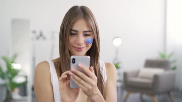 Portrait of young pleasant woman sitting at home using her mobile phone and smiling. Message box painted on girls face. Social media concept. Modern conversation style. - Footage, Video