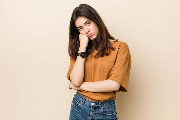 Young brunette woman against a beige background who feels sad and pensive, looking at copy space. - Foto, Imagen