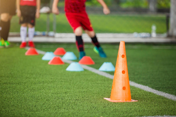 Orange marker cones on green artificial turf with blurry kid soc - Photo, Image