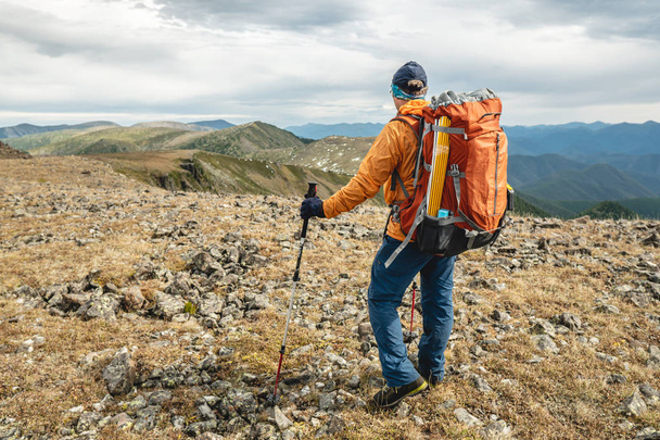 Man wandelaar met wandelstokken op zoek naar een bergvallei met heuvels bij zonnig weer. Reis en bereik het doel - Foto, afbeelding