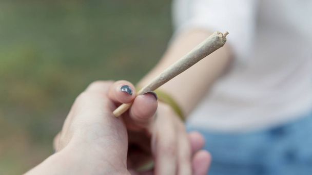Κοντινό μέρος των θηλυκών χεριών που κρατούν την άρθρωση μαριχουάνας, καπνίζουν canna - Φωτογραφία, εικόνα