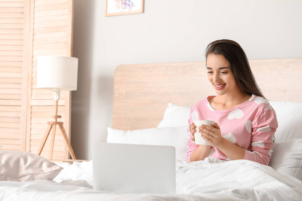 Morning of beautiful young woman with laptop and cup of coffee in bedroom - Foto, Bild