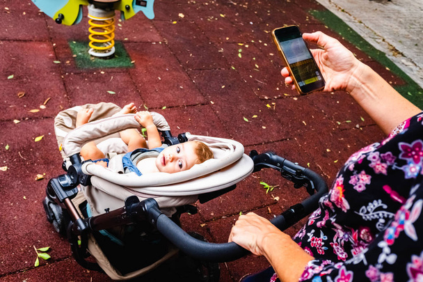 Mutter geht mit Baby spazieren, während sie abgelenkt ihr Smartphone benutzt - Foto, Bild