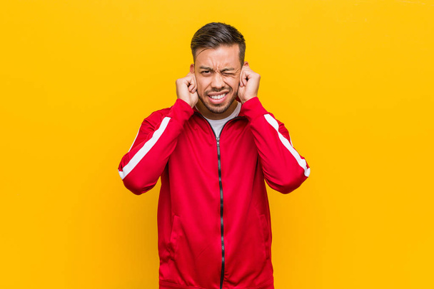 Young filipino fitness man covering ears with hands. - 写真・画像