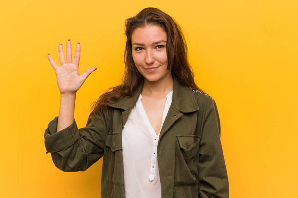 Молодая европейская женщина изолирована на желтом фоне улыбаясь весело показывая номер пять с пальцами
. - Фото, изображение
