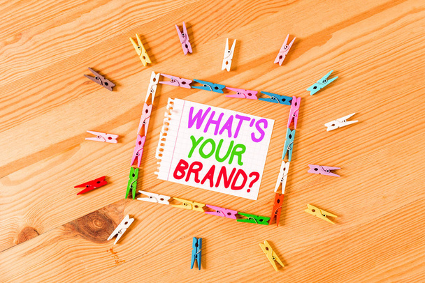Handschriftliches Textschreiben, was Ihre Markenfrage ist. Konzept bedeutet, nach dem Produkt-Logo zu fragen oder was Sie kommunizieren farbige Wäscheklammern Papier leer Erinnerung Holzboden Hintergrund Büro. - Foto, Bild