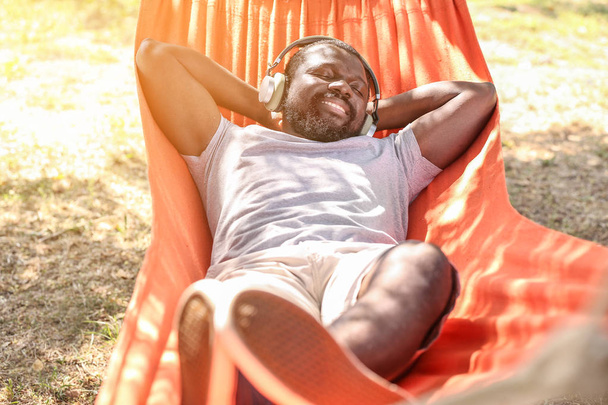 Hombre afroamericano escuchando música mientras se relaja en la hamaca al aire libre
 - Foto, Imagen