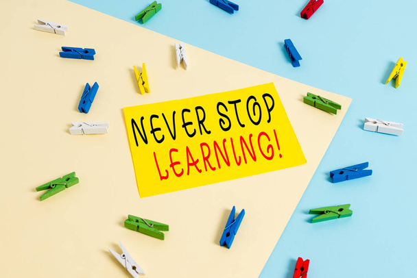 Szöveges jel mutatja Never stop learning. Fogalmi fotó tartani a tanuló egyre új ismereteket vagy anyagokat színes ruhacsipesz papír üres emlékeztető sárga kék padló háttér iroda. - Fotó, kép