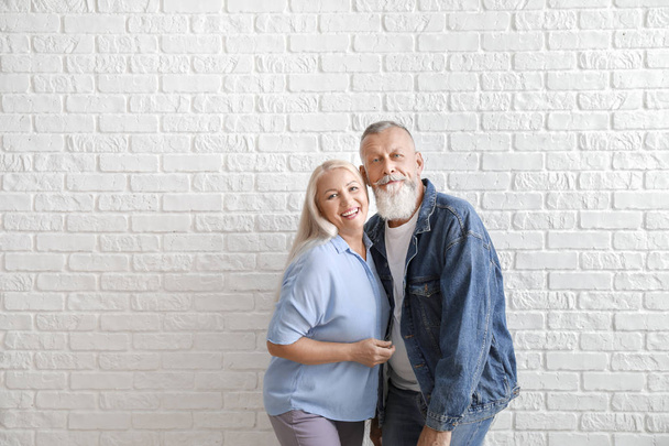 Feliz casal maduro contra parede de tijolo branco
 - Foto, Imagem