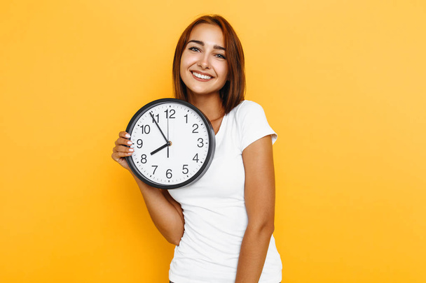 Young attractive woman with a watch on a yellow background - Foto, Imagem