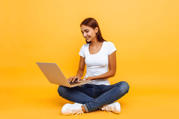 young woman sitting cross-legged using laptop isolated on yellow - Zdjęcie, obraz